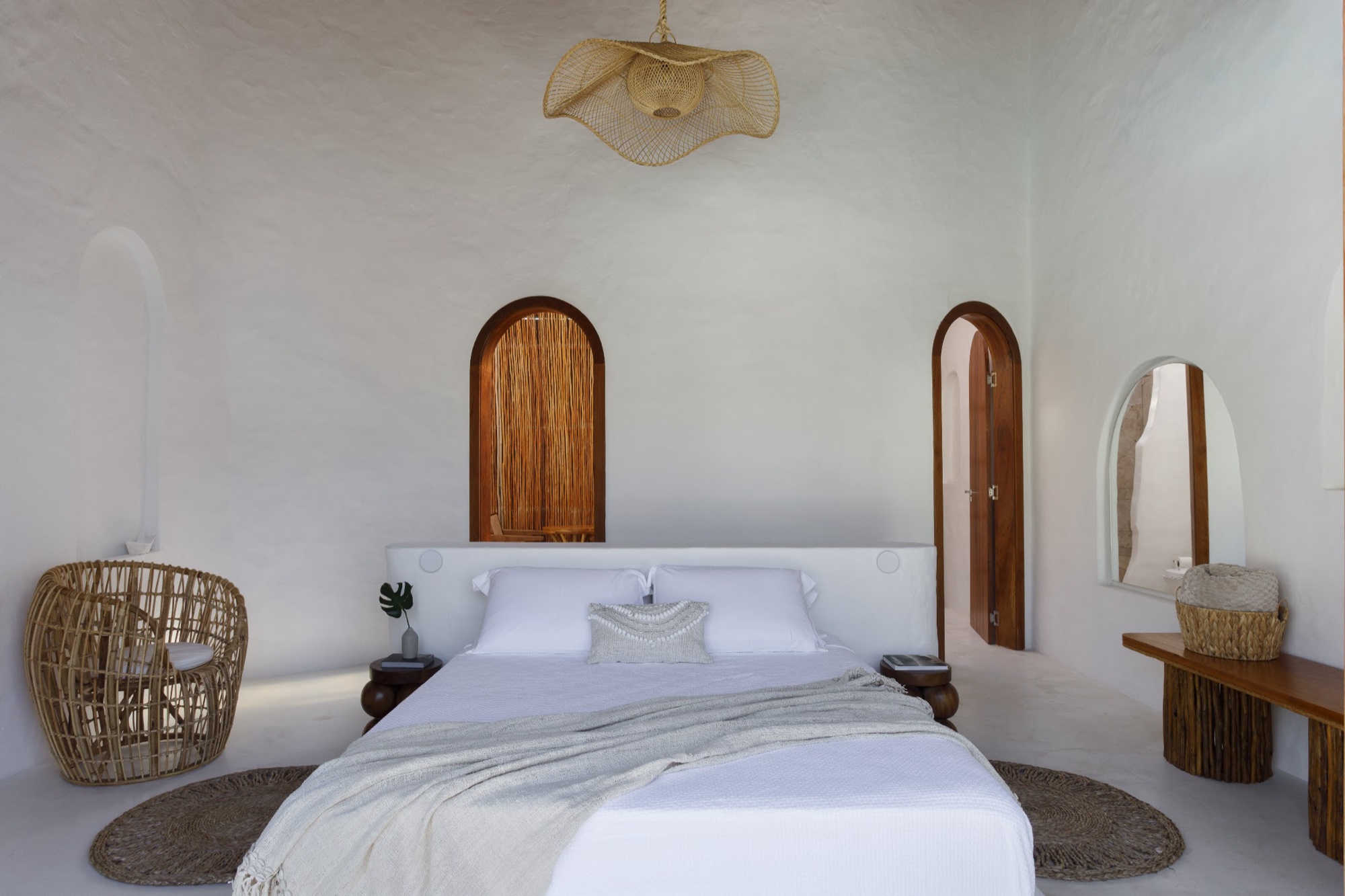 Bangalô Comfort: paredes curvas de cal com nichos em arco, poltrona de rattan e cama com manta de tricô